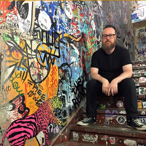 O diretor e roteirista Dennison Ramalho sentado nos degraus de uma escada A man is sitting on a set of stairs in front of a wall with graffiti on it