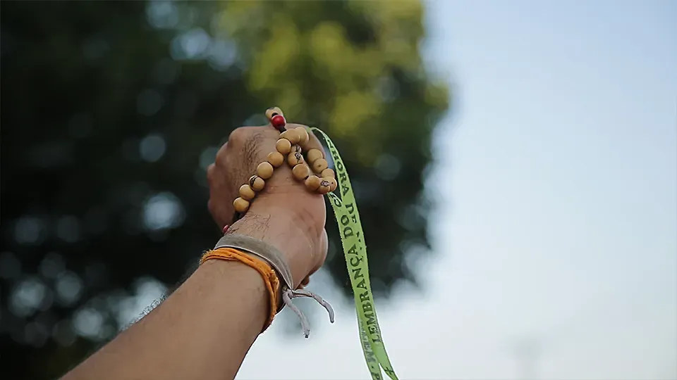 A person is praying with a rosary and a green ribbon that says ' esperanza ' on it