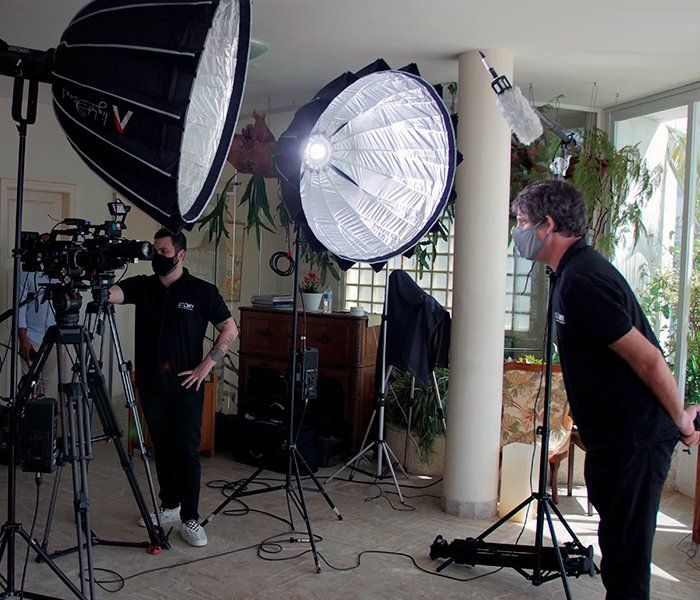 A man wearing a mask stands in front of a camera and a light that has the letter v on it