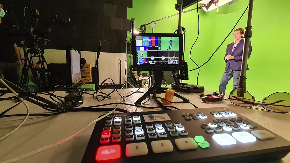 A man is standing in front of a green screen in a studio.