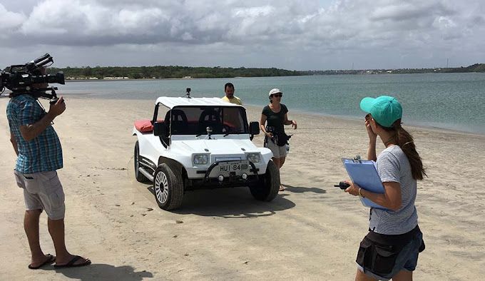 A group of people are standing on a beach in front of a buggy.