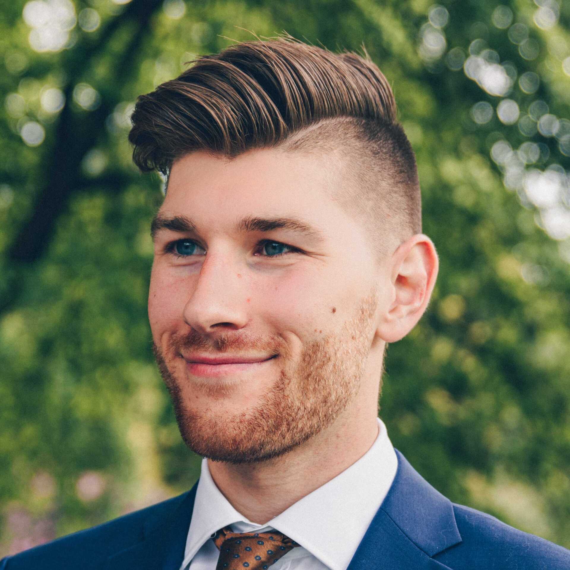 A man with a beard is wearing a suit and tie and smiling.