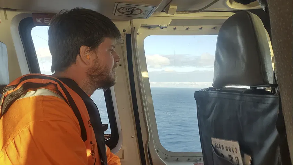 A man in an orange jacket is looking out the window of a helicopter.