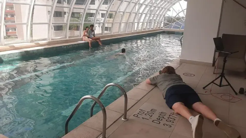 A woman is laying on the edge of an indoor swimming pool.