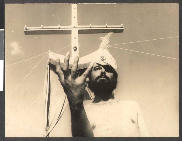 José Mojica Marins, também conhecido como Zé do Caixão, em cena do filme 'O profeta' A man is holding a cross over his head in a black and white photo.