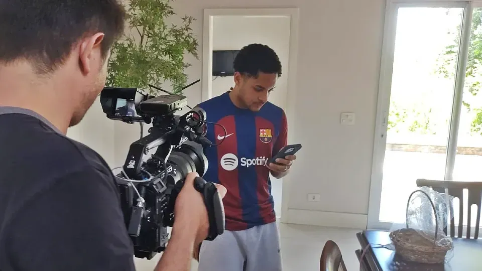 A man in a spotify shirt is being filmed by a cameraman.