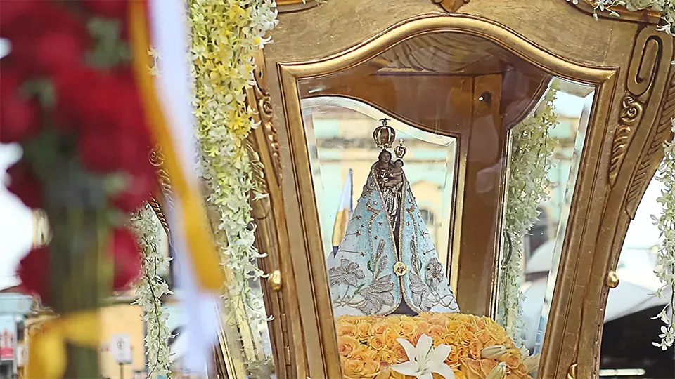 A statue of a woman in a blue dress is in a gold frame surrounded by flowers.