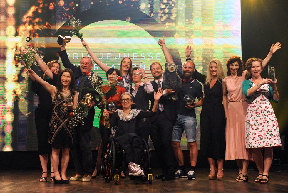 A group of people are standing on a stage with their arms in the air.