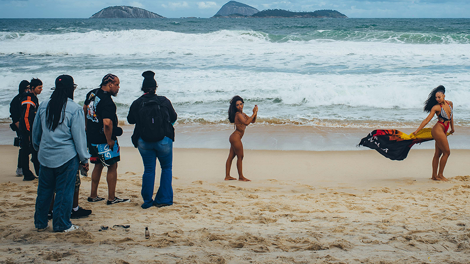 A group of people are standing on a beach taking pictures of a woman in a bikini.