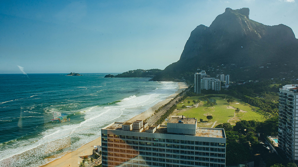 An aerial view of a beach with a mountain in the background and a large building in the foreground.