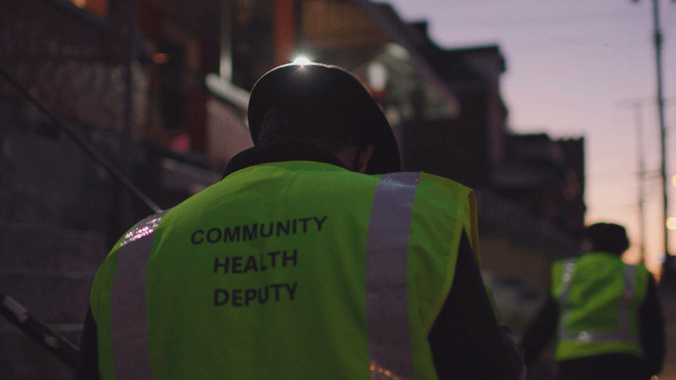 A man wearing a yellow vest with the words `` community health deputy '' on it.