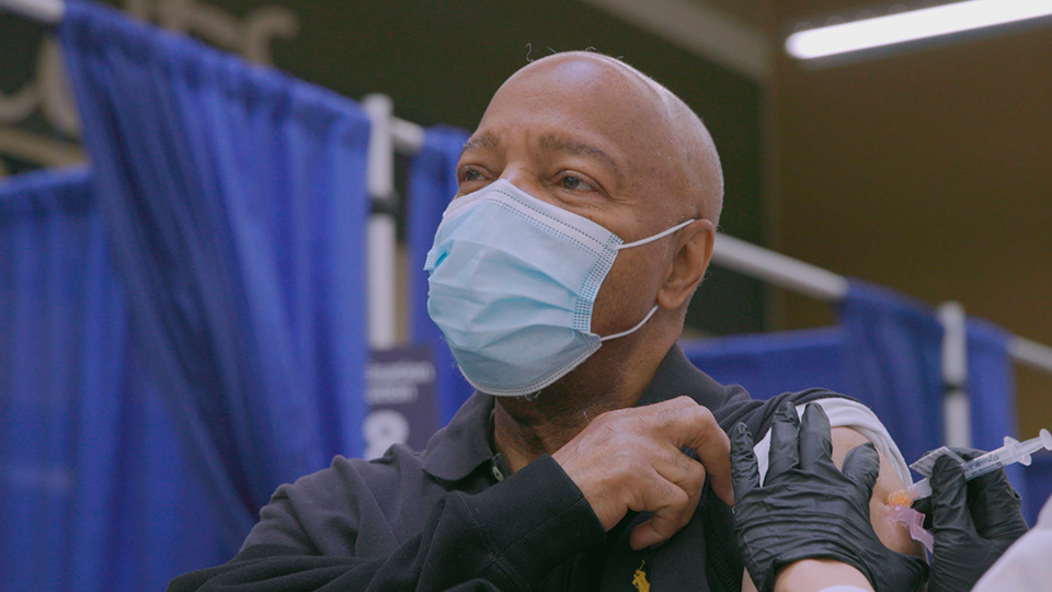 A man wearing a mask and gloves is getting a vaccine.