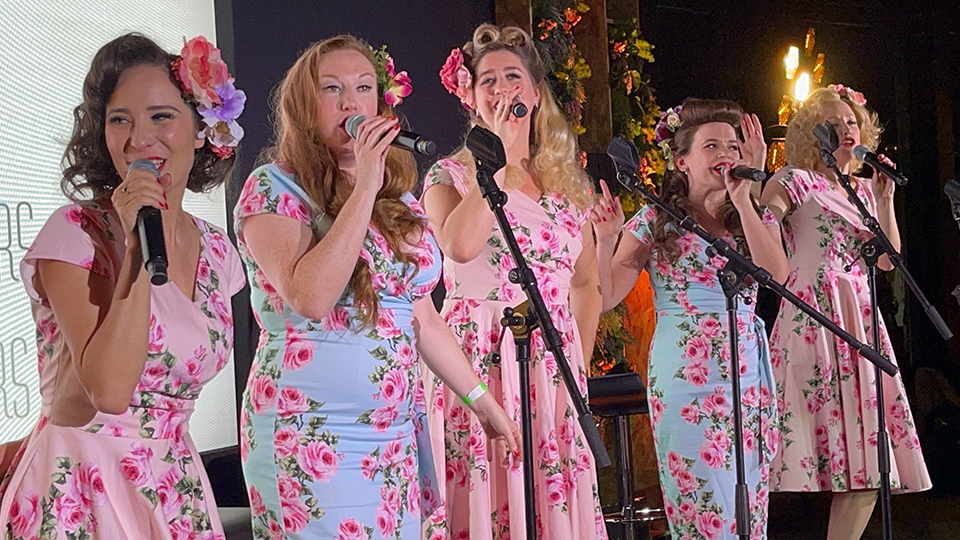 four women sing while holding microphones at night