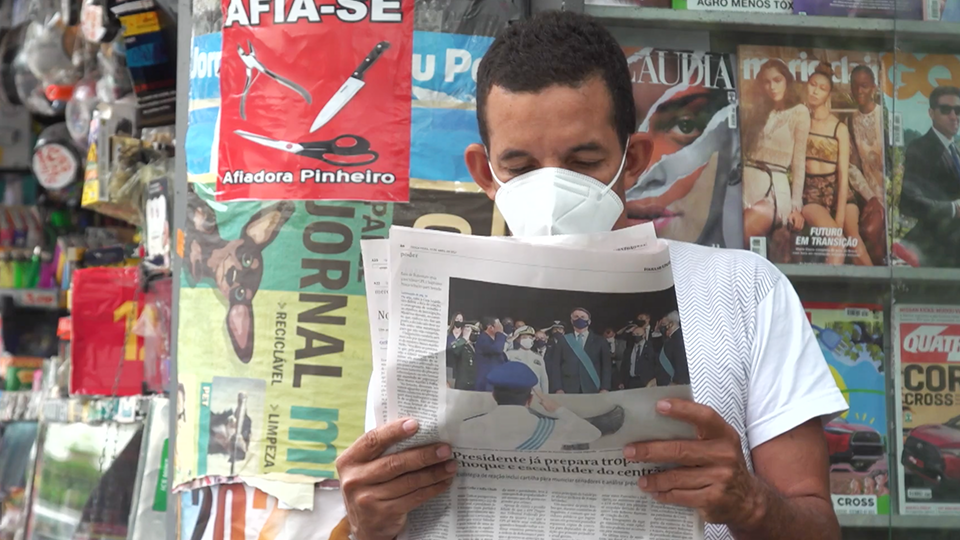 A man wearing a mask is reading a newspaper