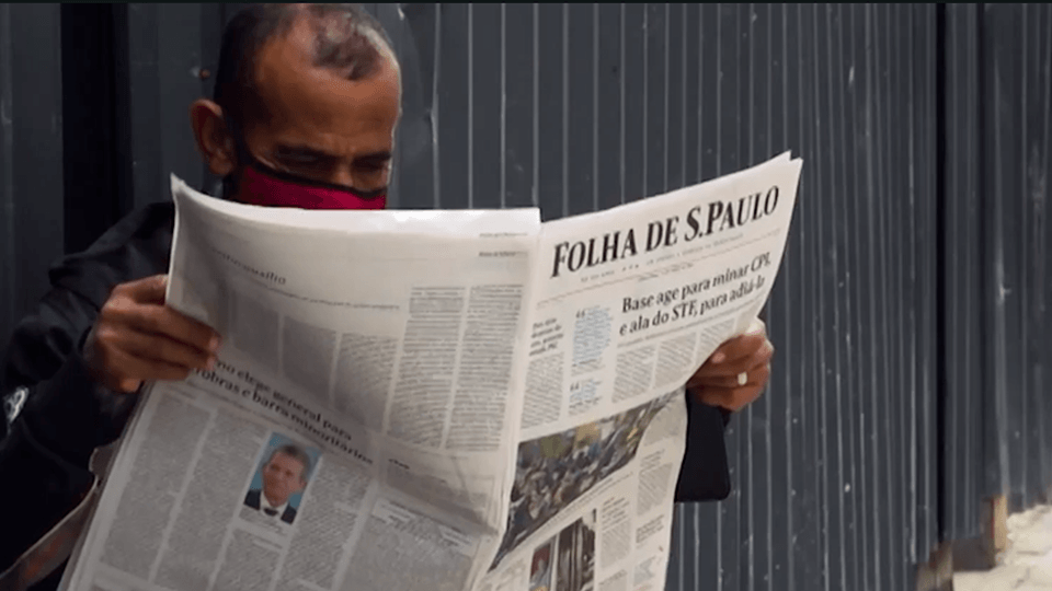 A man wearing a red mask is reading a newspaper