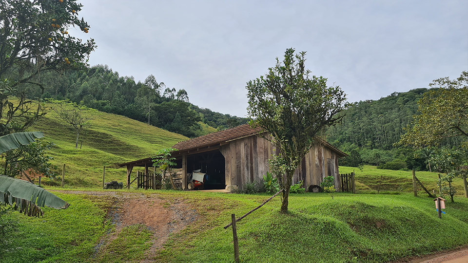 A wooden barn is sitting in the middle of a grassy field.