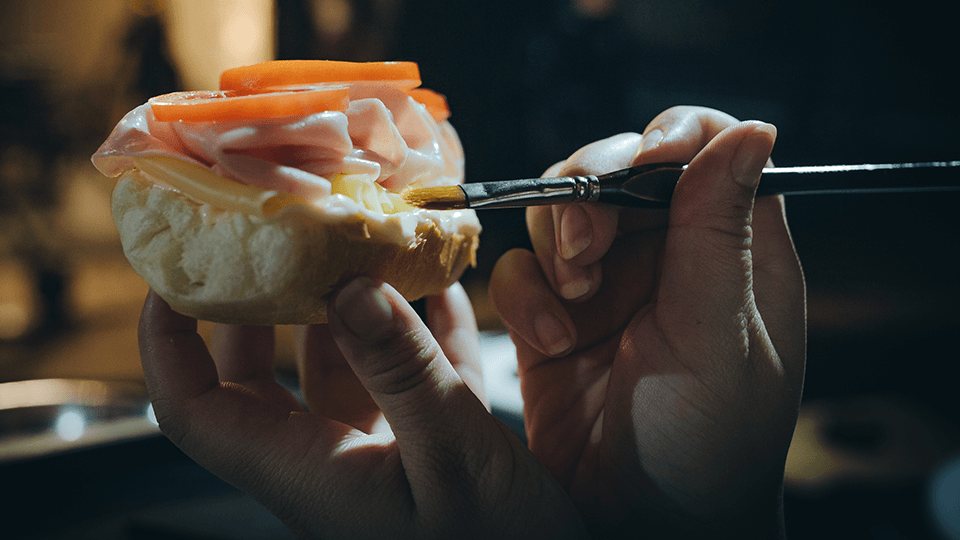 A person is painting a sandwich with a brush.