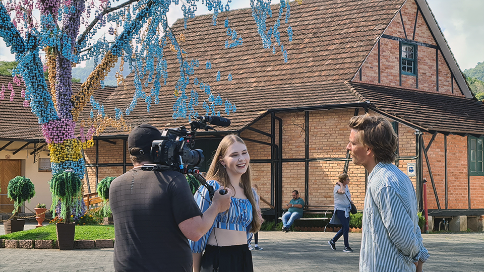 A man is holding a camera while talking to a woman in front of a brick building.