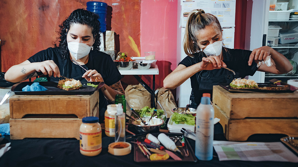 A view of the fields on a coffee farm in rural Brazil Two women wearing face masks are preparing food at a table.