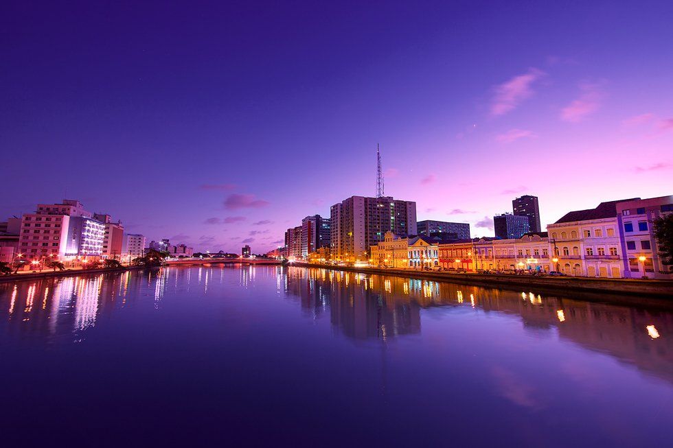 A city at night with a river in the foreground and buildings in the background.