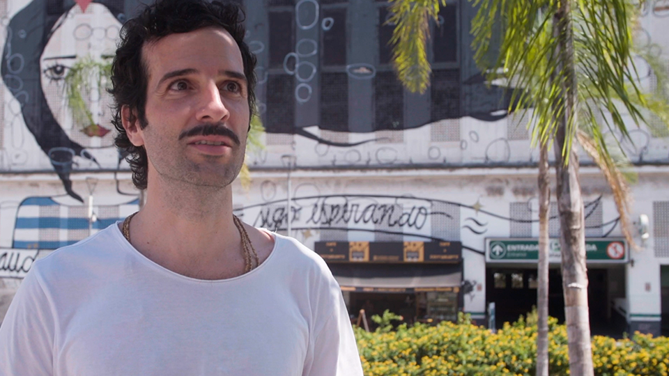 A man talks to a camera with an old building