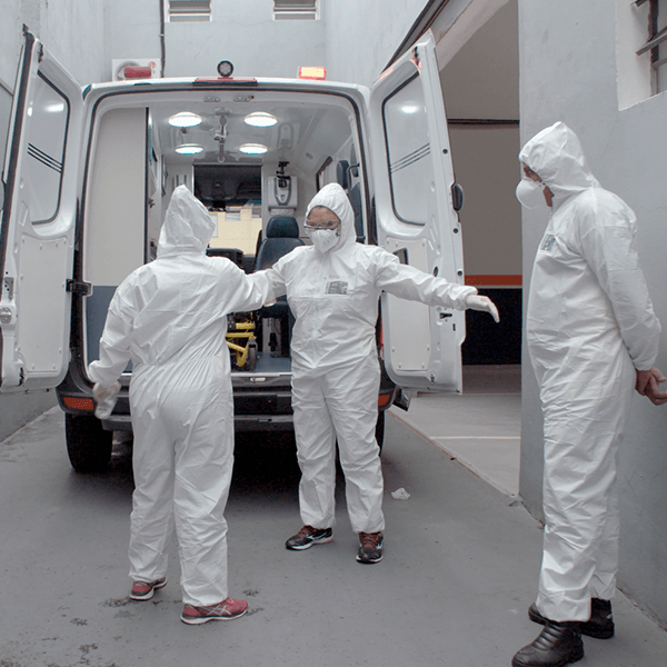 Three people in protective suits are standing in front of an ambulance