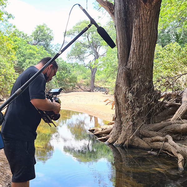 Story Productions crew is on location capturing the landscape where the macaws are preserved A man is taking a picture of a river with a camera.