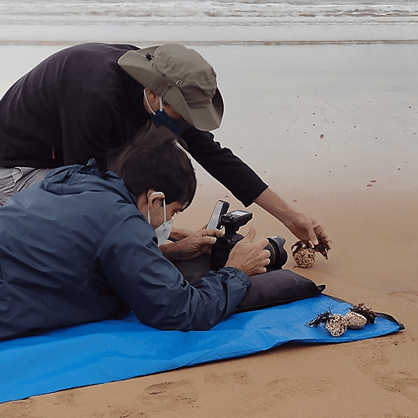 Two men are laying on a blue blanket on the beach