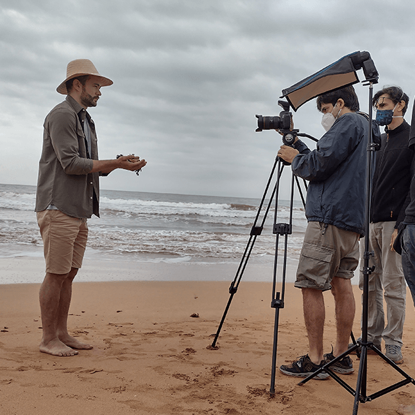 A man in a hat is talking to another man on the beach