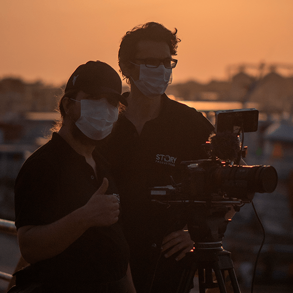 A man wearing a mask stands next to another man holding a camera