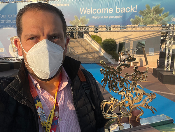 A man wearing a mask stands in front of a welcome back sign