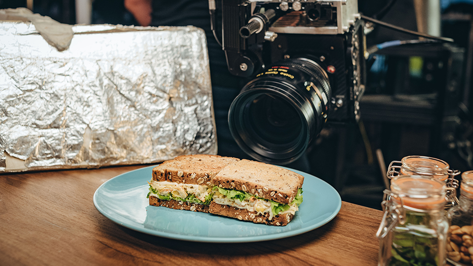 A sandwich is on a blue plate in front of a camera.