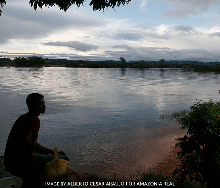 A man sits on the shore of a large body of water