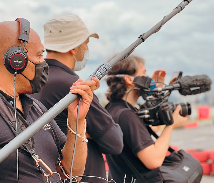 A man wearing headphones is holding a microphone while another man holds a camera