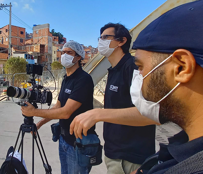 Three men wearing face masks are standing in front of a camera
