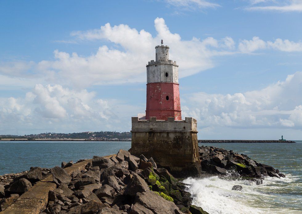 A red and white lighthouse is sitting on top of a rocky cliff overlooking the ocean.