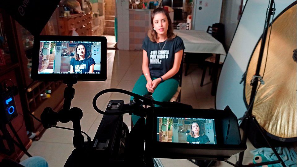 A woman is sitting in front of a camera in a room.