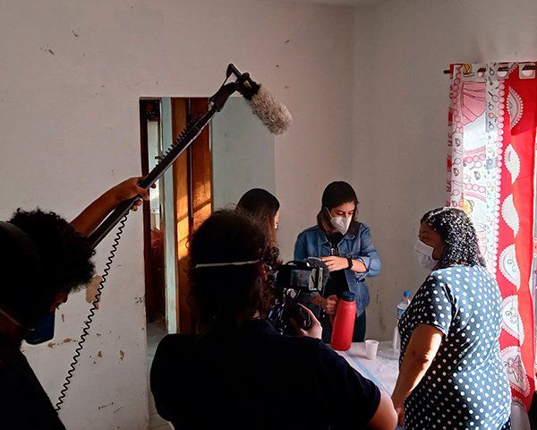 Story Productions crew films in a house while three women serve coffee A group of people are standing in a room with a microphone.