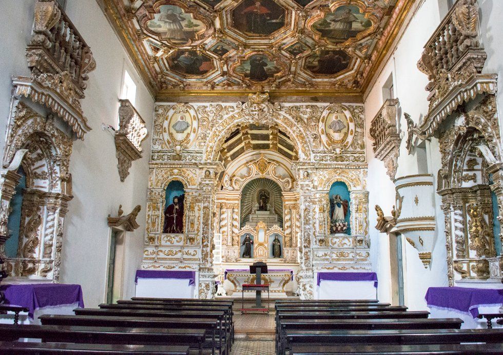 The inside of a church with wooden benches and a gold ceiling.