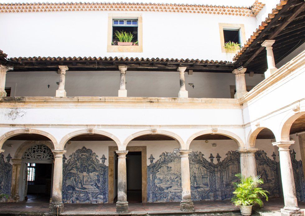 A courtyard of an old building with arches and blue and white tiles on the walls.