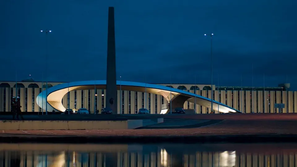 A bridge over a body of water with a building in the background at night.