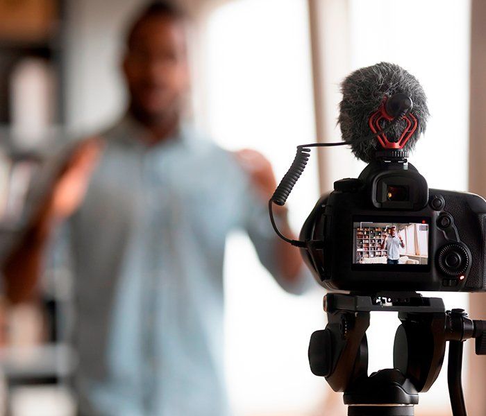 A man is standing in front of a camera with a microphone attached to it.