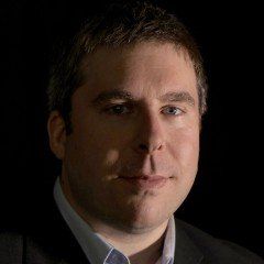 A man in a suit and tie is standing in front of a black background.