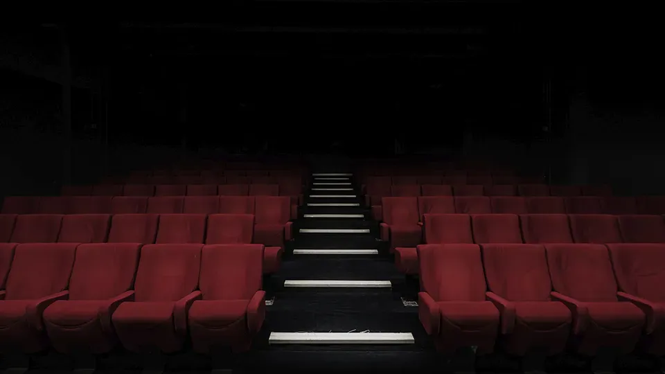 A row of red seats in an empty theater with stairs leading up to them.