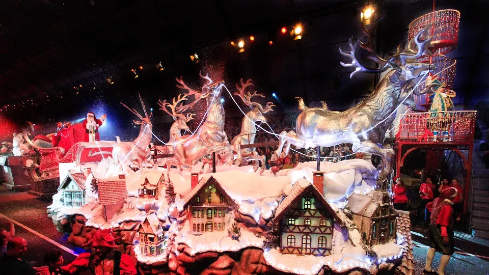 A group of people are standing in front of a christmas scene with reindeer and houses.