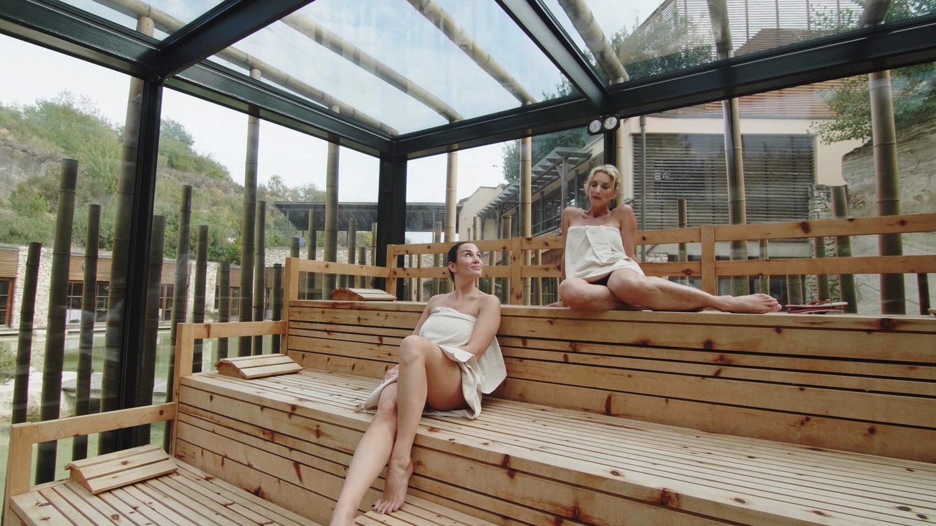 Two women are sitting on wooden benches in a sauna.