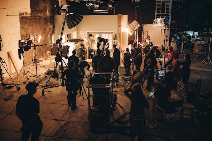 A group of people are standing in a room with a lot of lights and cameras.