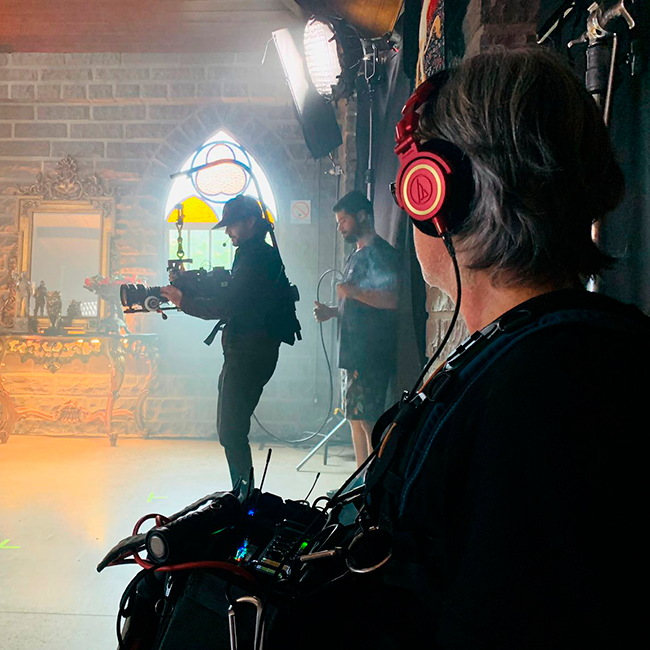 A man wearing headphones is standing in front of a camera.