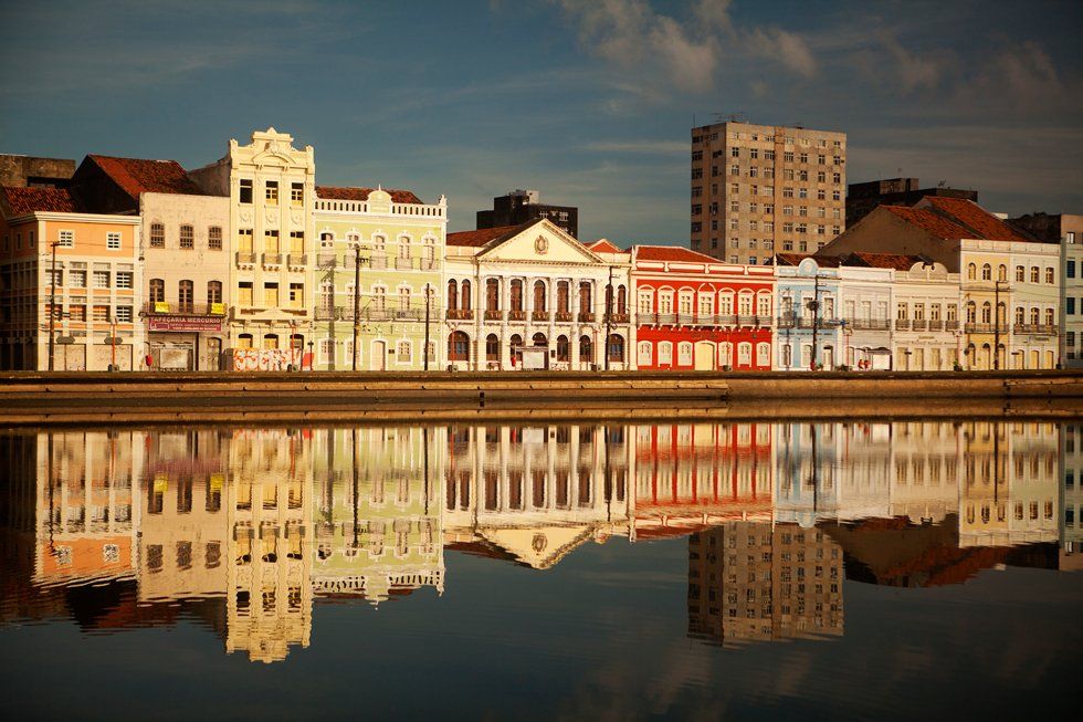 A row of buildings are reflected in a body of water.