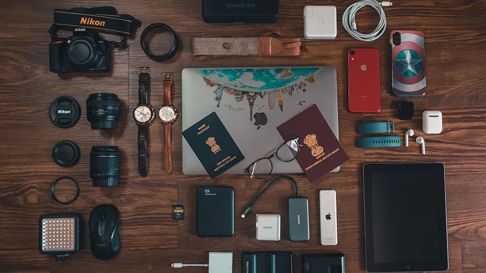 Equipos de filmación, electrónica y documentos de viaje sobre una mesa de madera.
